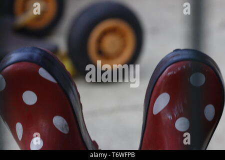 Image en couleur d'une vue rapprochée d'une paire de bottes pour enfants rouge à pois blancs. dans l'arrière-plan est un pneu jaune à partir d'un jouet. Banque D'Images