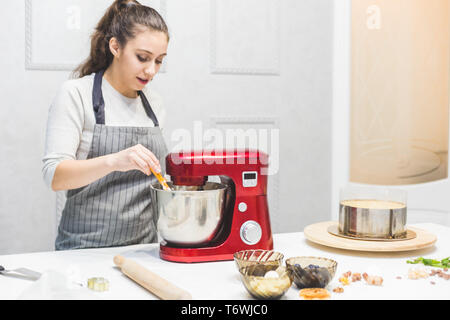 Jeune femme pâtissier bat la crème dans un bol en métal rouge dans un mélangeur électrique. Le concept de pâtisserie maison, la cuisine. Banque D'Images