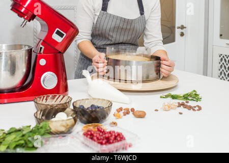 Jeune femme pâtissier bat la crème dans un bol en métal rouge dans un mélangeur électrique. Le concept de pâtisserie maison, la cuisine. Banque D'Images