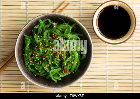 Salade d'algues Wakame graines de sésame et le piment de cayenne dans un bol sur un tapis de bambou Banque D'Images