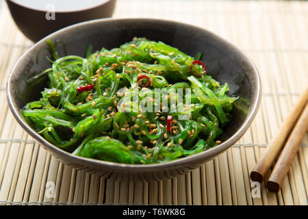 Salade d'algues Wakame graines de sésame et le piment de cayenne dans un bol sur un tapis de bambou Banque D'Images