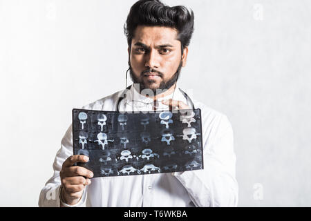 Beau jeune médecin dans une robe blanche avec un stéthoscope attentivement vérifie le cliché radiographique. Banque D'Images