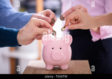 La main d'affaires Introduction de pièces en rose Tirelire In Office Banque D'Images