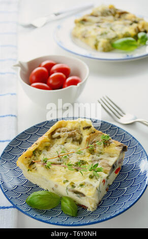 Quiche au fromage et aux champignons frais cuit tranches sur plaques bleu et blanc avec des tomates cerises. Format vertical de lumière naturelle. Banque D'Images