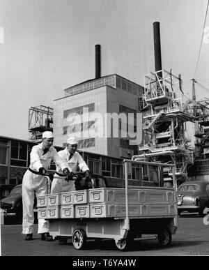 Portrait de deux travailleurs poussant un élément de combustible boîtes sur Dolly, réacteur avec le numéro 2 dans l'arrière-plan, la centrale nucléaire de Calder Hall, à Sellafield, Royaume-Uni, 1956. Image courtoisie du département américain de l'énergie. () Banque D'Images