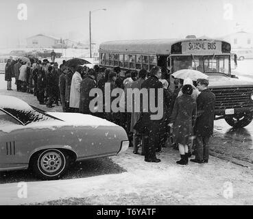 Une foule de personnes, se sont réunis à l'extérieur sur un jour de neige, attendant de monter à bord d'un autobus scolaire en route pour une cérémonie d'inauguration des travaux au Fermilab, Batavia, Illinois, 1968. Image courtoisie du département américain de l'énergie. () Banque D'Images