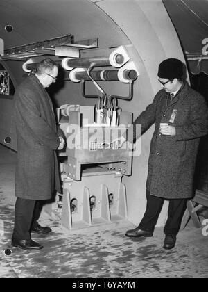 Deux hommes debout, en profil de pleine longueur, à la recherche d'un modèle à l'accélérateur de Fermilab proposé anneau principal, George Wheeler (droite) points à un aimant, Batavia, Illinois, le 2 décembre 1968. Image courtoisie du département américain de l'énergie. () Banque D'Images