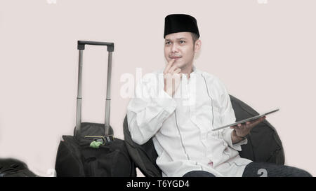 Portrait de bel asiatique musulman avec tête à assis sur table avec valise bagages et à l'aide de l'onglet Commander ticket pour le ramadan Aïd Mubarak Banque D'Images