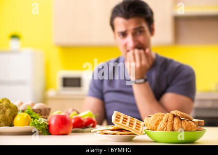 Homme avoir choix difficile entre les aliments sains et malsains Banque D'Images