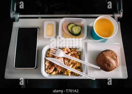 Service de repas à bord pour la classe économique du bac, de la viande avec des pâtes, des fruits, l'assaisonnement de la salade, concombre, un verre de jus et le beurre. focus sélectif. Banque D'Images