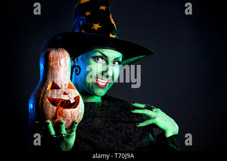 Sorcière avec peau verte tenue Halloween citrouille sculptée au fond sombre Banque D'Images
