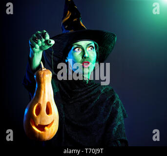 Sorcière avec peau verte holding carved Halloween Pumpkin lantern fond sombre Banque D'Images