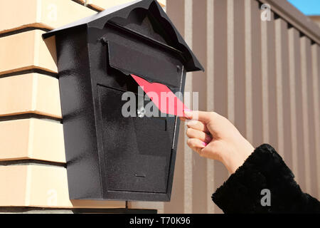 Woman putting lettre dans la boîte aux lettres à l'extérieur Banque D'Images