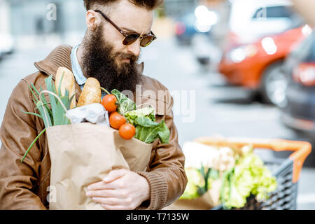 Heureux l'homme élégant avec les sacs pleins d'aliments frais et sains à l'extérieur près du supermarché Banque D'Images