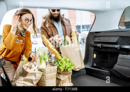 Jeune couple avec des sacs d'emballage des aliments frais dans le coffre de la voiture, vue de l'intérieur du véhicule Banque D'Images