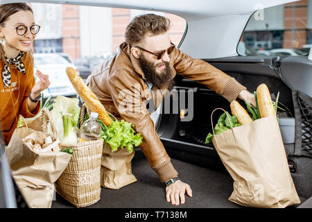 Jeune couple avec des sacs d'emballage des aliments frais dans le coffre de la voiture, vue de l'intérieur du véhicule Banque D'Images