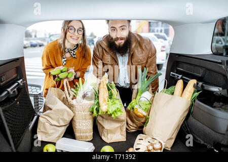 Jeune couple avec des sacs d'emballage des aliments frais dans le coffre de la voiture, vue de l'intérieur du véhicule Banque D'Images