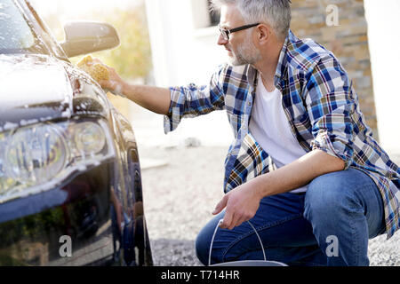 Homme mûr lave sa voiture avec une éponge savonneuse en entrée Banque D'Images