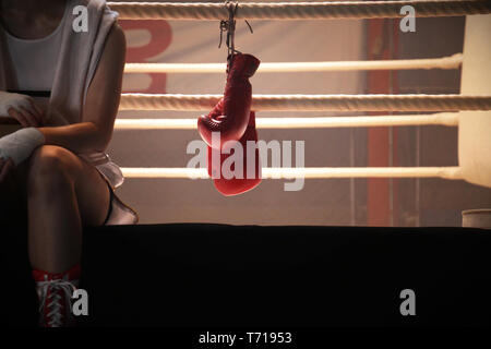 Un boxeur assis sur le bord du ring de boxe et des gants de boxe suspendu par la chaîne Banque D'Images