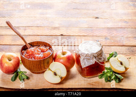 Bol en bois avec cuillère et petit pot en verre avec couvercle fermé avec du papier fait maison confiture de pommes et pommes et menthe verte sur planche en bois sur l'ancien rus Banque D'Images
