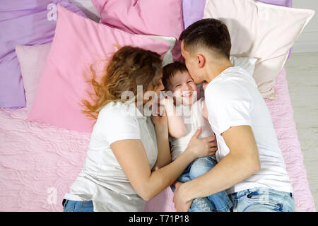 Portrait of happy young family au lit, maman, fils et papa sont embrasser et s'étreindre ensemble, de sourire et de visages joyeux. Lovely moments en famille. Banque D'Images