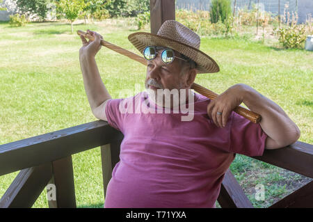 Portrait of happy senior man barbu à lunettes rondes reposant tout en étant assis sur la saison d'été à veranda Banque D'Images