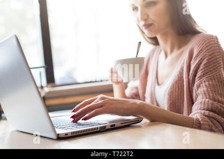 Belle jeune femme est assise à une table dans un café avec une tasse de café et bénéficie d'un ordinateur portable Banque D'Images