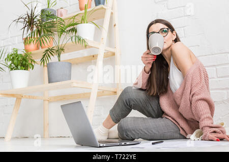 Jeune femme assise sur le sol dans un appartement scandinave intérieur avec un ordinateur portable, d'étudier le droit, freelance girl at work, étudiant l'apprentissage à distance Banque D'Images