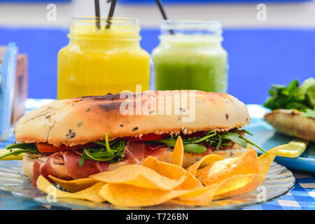 Sandwich de tomate, salade et du jambon avec du pain grillé et de jus. Miche de pain. Nappe à carreaux bleu. Salle à manger d'été. Banque D'Images