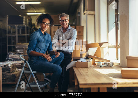 Smiling business partenaires réunis à l'entrepôt du vendeur en ligne. Jeune femme et homme mûr looking at camera and smiling at affaires d'expédition de baisse des Banque D'Images