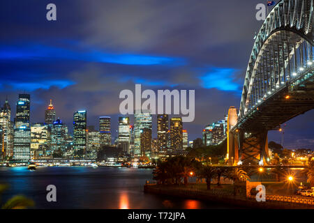 Vue latérale du monument architectural de Sydney Harbour Bridge et de la ville au coucher du soleil. Passage du pont illuminé se reflétant dans les eaux trouble Sydney, Nouvelle Banque D'Images