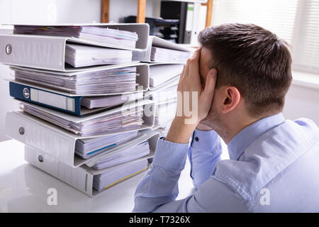 Vue arrière du souligné Businesswoman Pointing en face de dossiers empilés Banque D'Images