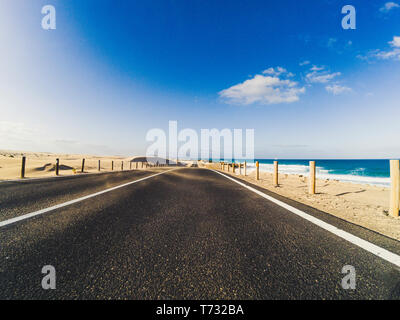 Long chemin road pour le transport en voiture concept avec désert et plage sur le côté - l'eau de mer et le bleu clair beau ciel en arrière-plan - motion Banque D'Images