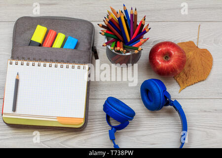 Les fournitures scolaires. Ouvrir un livre d'exercices sur-sac à crayons-feutres de couleur et de gabarit, écouteurs, Apple et support métallique avec des crayons de couleur sur w gris Banque D'Images