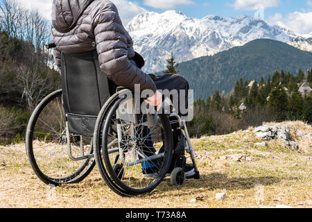 Photo gros plan de jeune homme handicapé en fauteuil roulant à l'extérieur dans la nature en montagne et la nature d'observation Banque D'Images