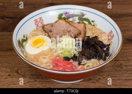 Tonkotsu Ramen au porc, lait de soja, bouillon de porc, les champignons noirs, les oeufs, les oignons, servi dans un bol en bois foncé, fond de table Banque D'Images