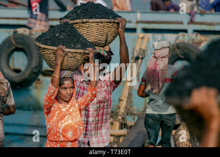 Station d'hommes et femmes de travailleurs sont considérés comme ils décharger le charbon avec des paniers de bambou de ferries au port de la rivière Buriganga à Dhaka, au Bangladesh. Banque D'Images