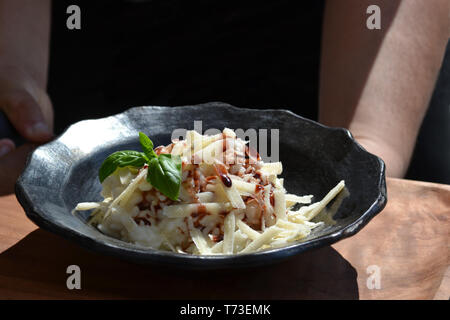 Risotto délicieux sur la plaque en céramique noire surmontée de copeaux de fromage parmesan, le persil et le vinaigre balsamique exposé sous le soleil clair par serveur. Banque D'Images