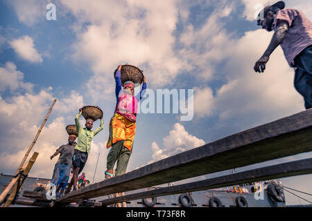 Station d'hommes et femmes de travailleurs sont considérés comme ils décharger le charbon avec des paniers de bambou de ferries au port de la rivière Buriganga à Dhaka, au Bangladesh. Banque D'Images