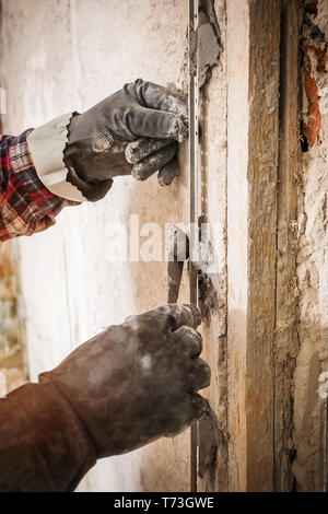 L'installation de balises de guidage métallique pour le remplissage et le nivellement des murs dans la réparation. Main recouvre le mur avec du plâtre. Banque D'Images