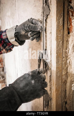 L'installation de balises de guidage métallique pour le remplissage et le nivellement des murs dans la réparation. Main recouvre le mur avec du plâtre. Banque D'Images