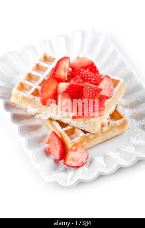 Belgique waffers avec du sucre en poudre et les fraises sur une plaque en céramique sur le tableau blanc. Des wafers. Banque D'Images