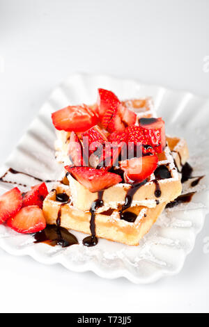 Belgique waffers avec du sucre en poudre, des fraises et du chocolat sur une plaque en céramique sur le tableau blanc. Des wafers. Banque D'Images