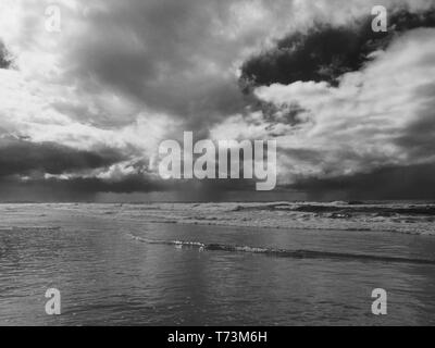 Temps orageux, nuages de tempête sombre se sont reflétés sur l'eau à la plage, alors que les nuages qui se profilent pleuvent sur la mer. Noir et blanc. Dramatique Banque D'Images