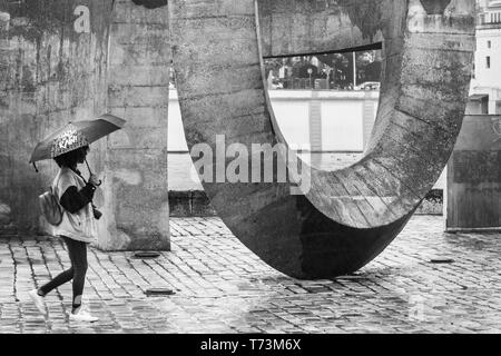 Une femme tenant un parapluie promenades par une grande sculpture sur une passerelle ; Séville, Espagne Banque D'Images