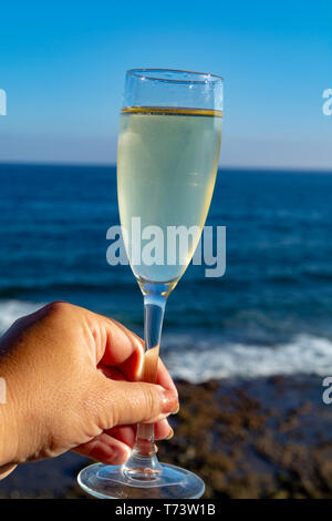 Main tenant le verre de Champagne, prosecco ou cava, terrasse extérieure avec vue sur la mer close up Banque D'Images