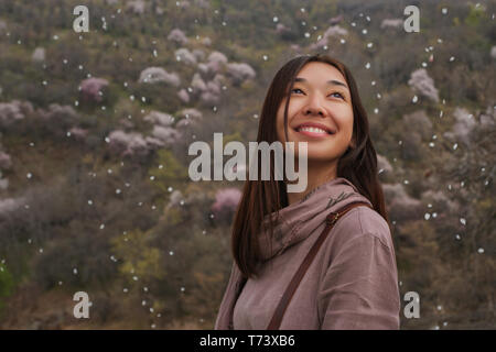 Asian girl en plein air au printemps. Duvushka sourit à la recherche. Pétales d'arbres en fleurs voler autour de lui. Sur la fille d'une longue robe de lin Banque D'Images