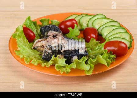 Morceaux de sardine iwashi sur des feuilles de laitue avec des tomates rouges. La plaque avec les sardines sur fond de bois. Banque D'Images