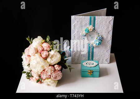 Un bouquet de roses roses et de pivoines blanches se trouve sur une surface blanche à côté du cercueil et une carte postale sur un fond noir Banque D'Images