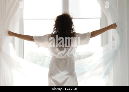 Matin de belle jeune femme ouvrant les rideaux dans la chambre Banque D'Images